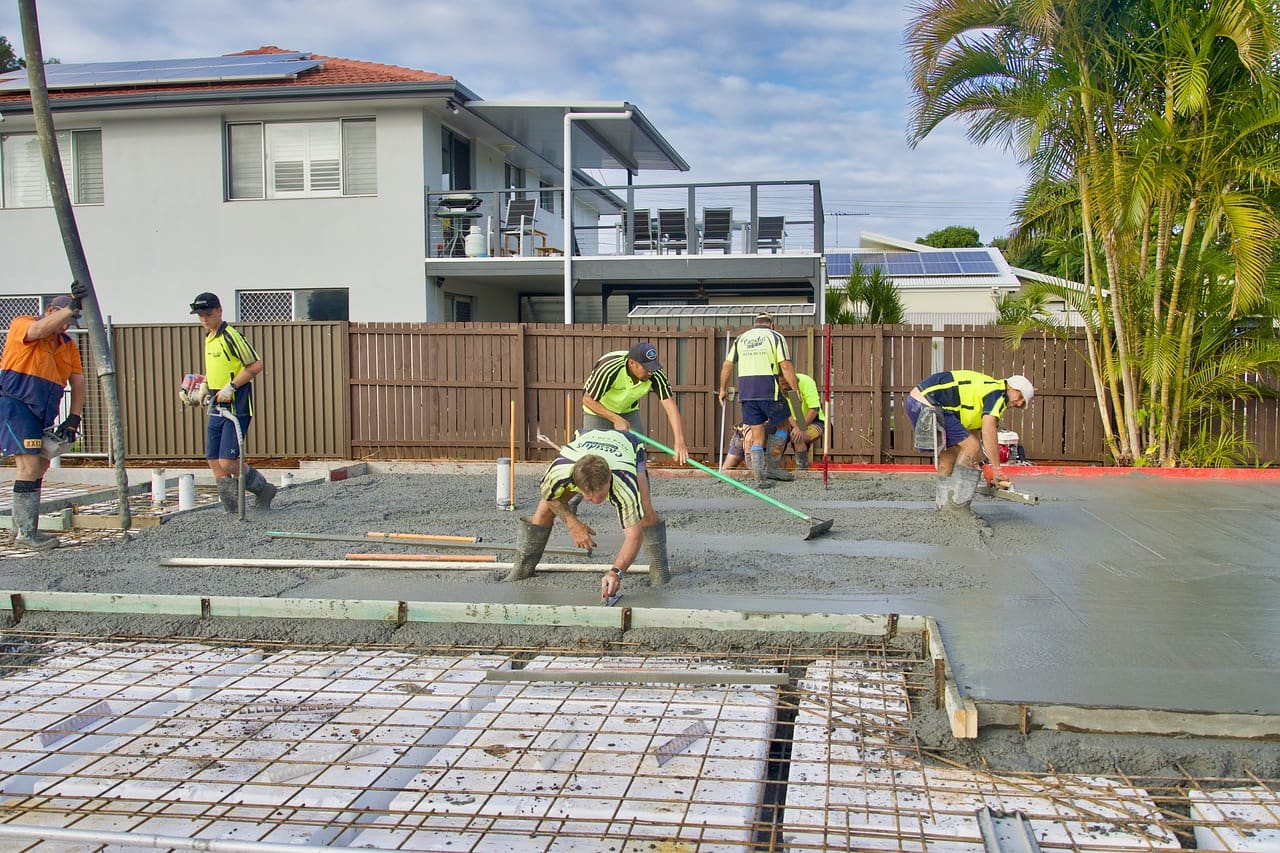 A group of men working on concrete in front of houses.